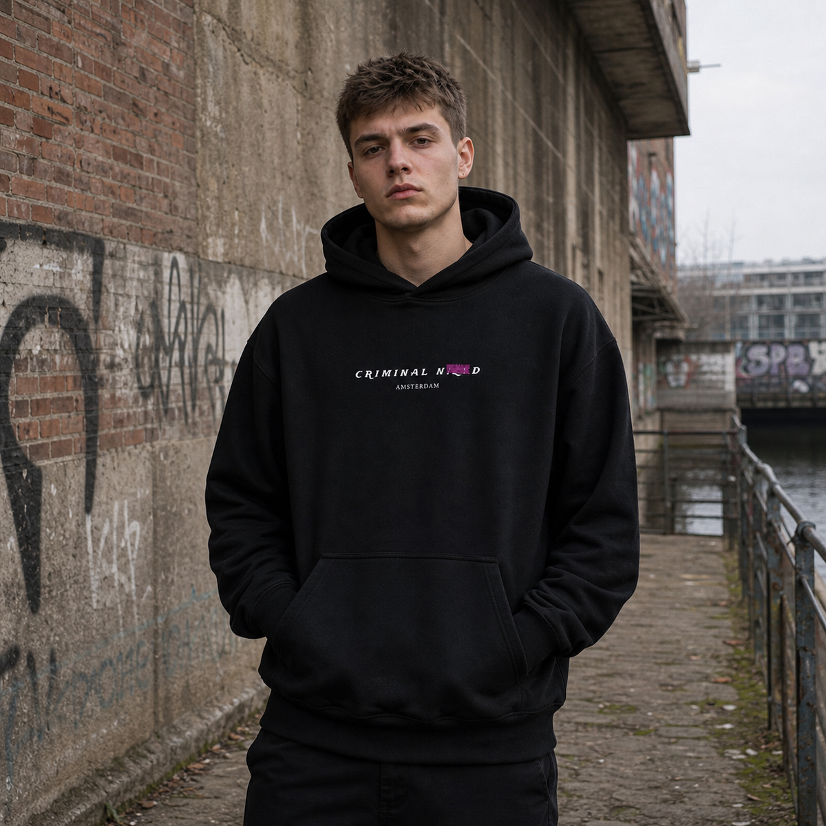Criminal Amsterdam Hoodie am männlichen Model mit Frontprint am Berliner Industriekanal – KI-generierte Darstellung