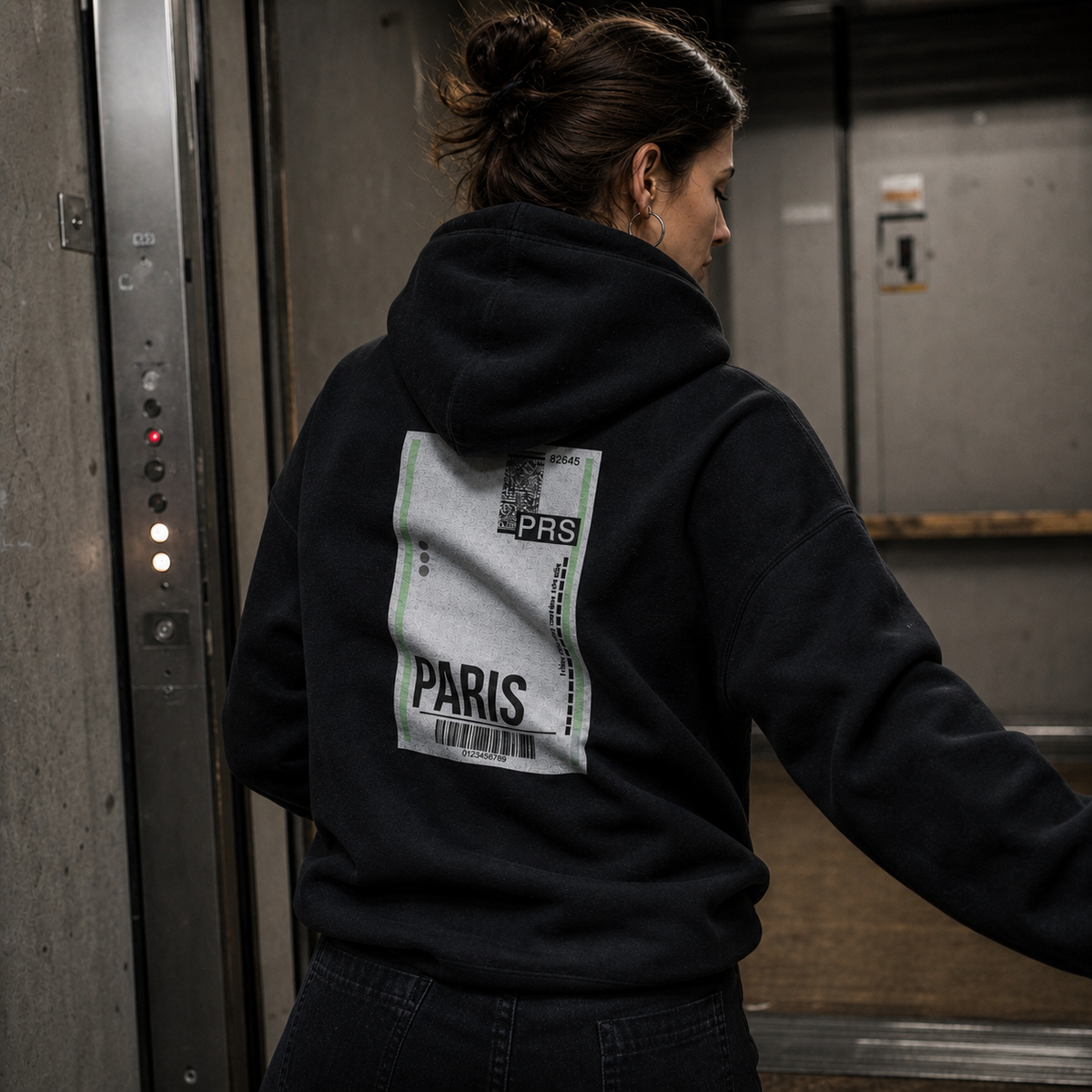 Not From Paris Madam Hoodie am weiblichen Model mit Backprint in einem Berliner Lastenaufzug – KI-generierte Darstellung